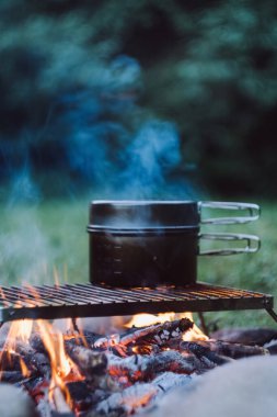 Akşamları, güzel sakin kamp ateşinin üzerinde siyah tencerenin yakın çekimi. Sıcak bir gecede şenlik ateşi yakmak. Kamp ortamı, doğa ve açık hava yaşam tarzı konsepti. Yaz tatilinde hızlı yemek kampı.