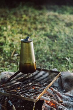 Güneş doğarken ya da batarken yeşil yaz parkında sıcak şenlik ateşi üzerinde gayzer kahve makinesinin yakın çekimi. Kamp ortamı, doğa ve açık hava yaşam tarzı konsepti. Yazın kamp ateşi, sıcak kahve.