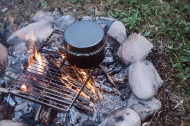 Akşam vakti, sakin bir kamp ateşinin üzerinde siyah bir tencerenin yakın çekim görüntüsü. Sıcak bir gecede şenlik ateşi yakmak. Kamp ortamı, doğa ve açık hava yaşam tarzı konsepti. Hızlı yemek kampı.