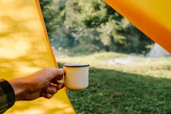 夏天的早晨 年轻的高加索人坐在黄色的帐篷里 坐在篝火和绿色的森林里徒步旅行 喝着热咖啡 惊醒了人们的视线 — 图库照片