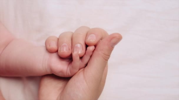 就在上面看去 可爱的年轻妈妈牵着新生儿的手 而宝宝则躺在舒适的白色床上 母亲的爱和照顾 对儿童的保护 幼儿概念 — 图库视频影像