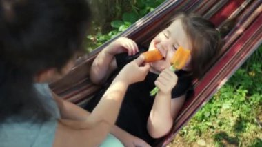 İki gülen çocuk sıcacık hamakta uzanmış taze havuç yiyor şakacı komik kız kardeşler sıcak hava haftasonunun tadını çıkarıyor. Vitamin ve mineral açısından zengin tam teşekküllü bir diyet. Çocukluk kavramı