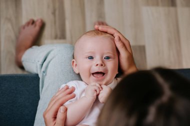 Sevecen bir annenin kucağında kucağında gülümsemesi küçük tatlı bebek, sevgi dolu genç bir anne kanepeye oturan yanaklarına dokunur ve başını okşar. Çocukluk anları kavramı
