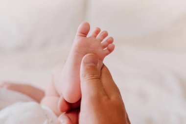 Anne ve babası, yeni doğmuş bebeğin ayaklarıyla sıcak beyaz bir yatakta uzanıyorlar. Bilinmeyen baba yeni doğan bebeğe ayak masajı yapıyor. Baba ve küçük çocuk. Mutlu Aile kavramı. Terfi içeriği için boşluk kopyala