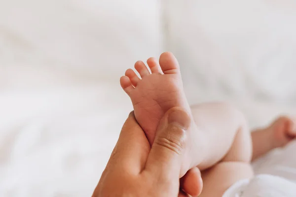 Dad massaging infant bare foot, preventive massage for newborn. Close up of father hands giving relaxing massage to small feet baby after daily bath in routine before going to sleep. Newborn baby care