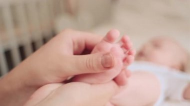 Bilinmeyen anne masajları bebek ayağı, evdeki rahat yatakta uzanmak. Mutlu aile çocuğu bebek konsepti. Çocuk masajı ve doktor annenin bakımı. Ayak masajı güven ve sevgi hissi yaratır.