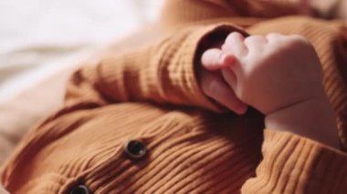 Evde yumuşak yatakta uzanan, saf ve rahat çarşafta dinlenen, tatlı, küçük, sevimli bebek ellerini kapat ve sakinliğini hisset. Kahverengi elbiseli bebek. Seçici odak