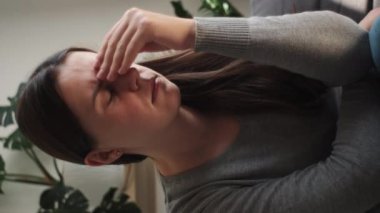 Kafasına dokunan, başı ağrıyan, migreni olan, evdeki kanepede oturan yorgun bir kadının dikey videosu. Bunalımlı üzgün kadın kayıpla, kederle, travmayla başa çıkıyor. Sinir krizi, kriz konsepti