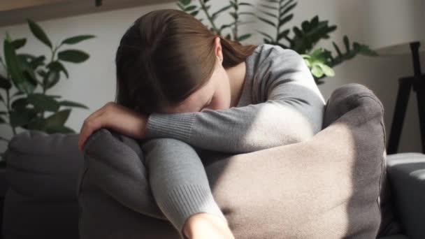 不幸な孤独な落ち込んだ若い白人女性が家でソファに座って 灰色の枕 うつ病 個人的な生活のトラブル 結婚の分裂 問題の概念に顔を隠しました — ストック動画