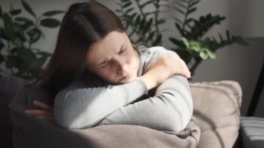 Akıl sağlığı konsepti. Kanepede ya da kanepede oturan depresyondaki üzgün genç kadın, yüzünü yastıkla kaplıyor. Zorluk, başarısızlık ve yorgunluk. Düşünceli endişeli depresyon evde yalnız hissediyor