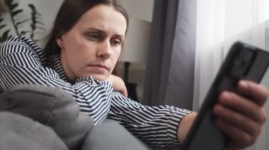Endişeli genç bir bayan cep telefonu kullanıyor, kötü haberler alıyor, sorun çıkarıyor, başka yere bakıyor. Ciddi düşünceli bir kadın elinde akıllı telefon, evinde koltukta oturuyor, internette sohbet mesajları, e-postalar ve mesajlar üzerine düşünüyor.