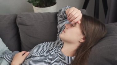 Depresyondaki genç kadın evinde kanepede uzanmış baş ağrısı yorgunluğu yalnızlık hissediyor. Üzgün, hasta, migren endişesi çeken, stresten sonra kanepede dinlenen, uykulu bir kadın.