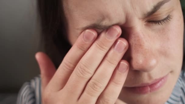 一个疲惫而不快乐的年轻女人坐在沙发上擦拭鼻梁 感到很不自在 因视力模糊 眼睛紧张 疼痛而沮丧的高加索女性 — 图库视频影像
