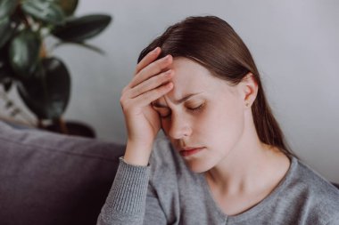 Yorgun ve stressiz bayan evdeki kanepede otururken depresyona giriyor. Kafası ağrıyan genç bir kadın. Baş ağrısı. Migren.