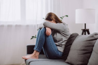 Mutsuz, kaygılı, 25 'lik esmer kadın. Oturma odasındaki koltukta diziyle oturuyor. Kalbi kırık, depresyondaki bir kadın.