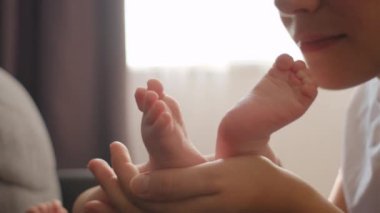 Sevecen, genç ve sevgi dolu bir annenin evdeki rahat koltukta uzanan küçük ayakları öpmesi, yeni doğmuş bir bebeğin minik ayak parmakları. Çocukla, anneyle ve çocuğuyla duygusal anlar, bakım konsepti