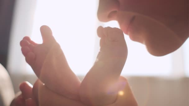 充满爱心的年轻母亲亲吻着可爱的新生儿的小脚 坐在舒适的沙发上 对婴儿 快乐的母亲 儿童保育的理念表达着诚挚而亲切的感激之情 — 图库视频影像