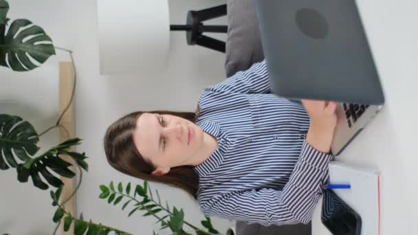 年轻博客女孩的垂直照片 作者写文章 坐在家里的办公桌旁 在笔记本电脑上打字 女人远视 触摸下巴 思考文字 用互联网技术工作 — 图库视频影像