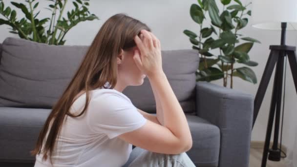 忧心忡忡的年轻女性坐在卧室沙发边的地板上 担心个人问题 一个人在家对戒除酗酒成瘾的焦虑妇女感到紧张 — 图库视频影像