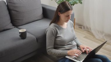 Evde dizüstü bilgisayarla çalışan beyaz, sevimli bir kadın evdeki sıcak salonda rahat bir yerde oturuyor. Çekici 25 'lik genç bayan bilgisayar ve çevrimiçi küçük işletme faaliyetlerinde çalışıyor.