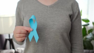 Erkekleri destekleyen sembol. Kadın elinin yakın çekimi oturma odasında duran küçük mavi kurdeleyi gösteriyor. Seçici odaklanma. Sağlık, Uluslararası erkekler, Baba ve Dünya Kanser Günü konsepti