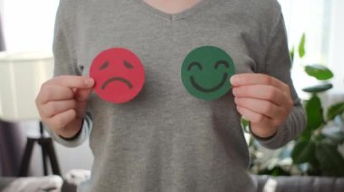 Odada elinde mutlu ve kızgın bir yüz kâğıdı tutan kadın ellerini kapat. Geri bildirim derecesi, duygusal zeka, denge duygu kontrolü, zihinsel sağlık değerlendirmesi, bipolar bozukluk konsepti