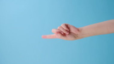 Kadın elinin dikey videosu hiçbir şey göstermiyor. Mavi stüdyo arka plan duvarında reklam ve tasarım için fotokopi alanı var. Onaylamayan jest. Reklam alanı, maket. Parmak işareti.