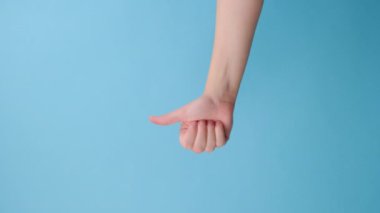 Dikey videoda kadın baş parmak hareketi yapıyor, onay ya da anlaşma gösteriyor, mavi arka planda izole edilmiş ve reklam için fotokopi alanı var. Vücut dili kavramı. El işareti. Jest gibi