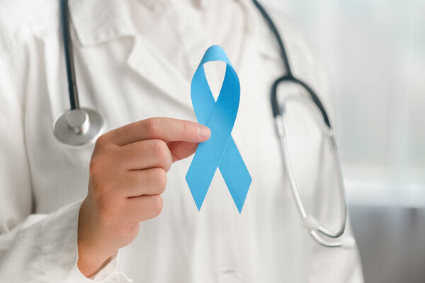 Close up of unrecognizable female doctor in uniform with stethoscope holding blue ribbon awareness. Men's health and Prostate cancer awareness campaign in November month. Symbol of medical issues