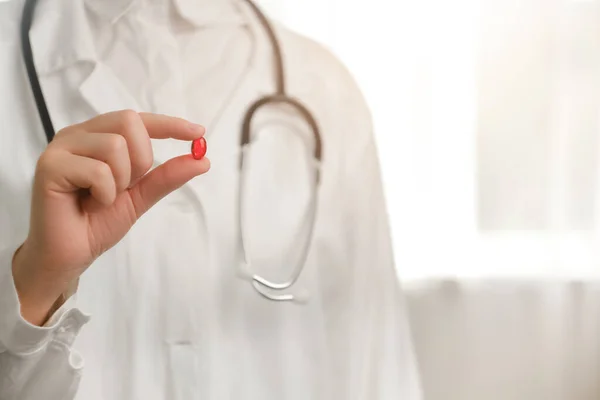 Supplements for stronger immune system. Close up of young woman doctor hand holding one red single pill, nurse wearing white coat and stethoscope. Medical, pharmacy and healthcare concept