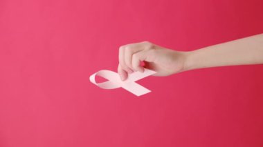 Kırmızı arka plan duvarında izole edilmiş pembe kurdeleleri tutan bir kadının dikey videosu. Göğüs kanseri farkındalığı, karın kanseri farkındalığı ve Ekim Pembe Günü, dünya kanser günü.