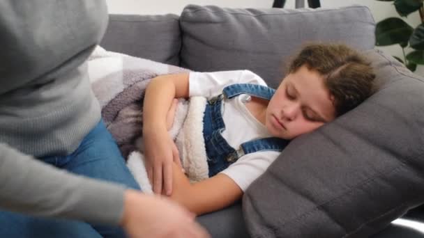 心配した若い母親は 娘の高体温をチェックし 額に触れ 温度計を保持しています 悲しい病気の少女がソファーに横たわり インフルエンザ 熱に苦しんでいます 子供のコンセプト — ストック動画