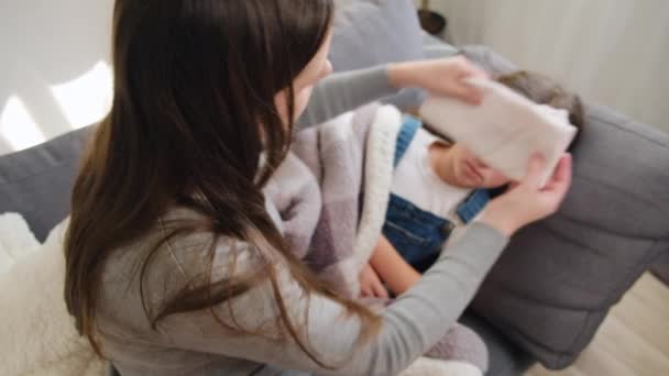 母親を世話するという選択的な焦点は 自宅でソファーに横たわる高体温の女性の頭にタオルを置きました 愛するママは病気の娘の世話をします チャイルドケア キッズヘルスケアのコンセプト — ストック動画