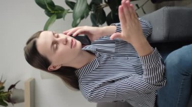 Sevimli bir kadının telefonda kişisel sohbetini yaptığı dikey video, arkadaşınla hafta sonu planlarını paylaş, koltukta oturup keyifli sohbetler yap. Cep telefonu operatör hizmetleri kullanılarak uzaktan iletişim