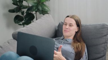 Çekici, genç bir kadın dizüstü bilgisayarla kanepede dinleniyor, video görüşmesi ile hoş sohbetler ediyor, hafta sonu boş zamanlarında haberleri paylaşıyor, evdeki kanepede uzanıyor.