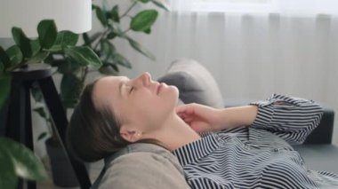 Güzel genç bir bayan, evinde rahat bir koltuğa oturmuş, kafasını yastığa koyuyor, temiz hava soluyor, modern oturma odasında dinleniyor. İklim kontrolü, yorgunluk giderme kavramı