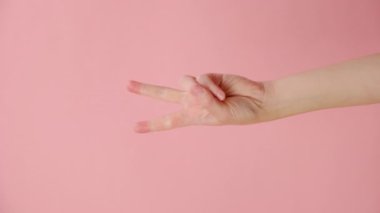 Kadın elinin parmak vücut dili ile kazandığı jestlerin dikey görüntüleri, pembe stüdyo arka plan duvarında izole edilmiş bir poz ve içeriği için fotokopi alanı. V işareti. Barış zafer kavramı