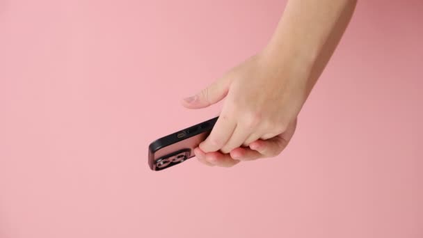スマートフォンを使用した女性の手の垂直ビデオは プロモーションコンテンツのコピースペースを備えたスタジオのパステルピンク色の背景壁の上に隔離されています 携帯電話を持っている未知のビジネスマン — ストック動画