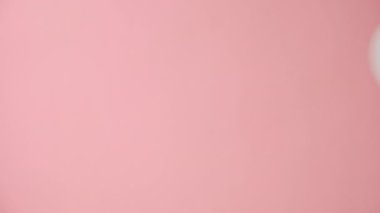 Büyük beyaz kağıt anahtarı tutan bir kadının dikey görüntüleri stüdyodaki pastel pembe arka plan duvarının üzerinde izole edilmiş bir şekilde duruyor ve promosyon içeriği veya tasarımı için fotokopi alanı mevcut. Kira ve emlak kavramı