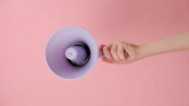 Mor megafonu tutan bir kadının dikey görüntüleri stüdyodaki pembe renkli arka plan duvarında reklam ve tasarım için fotokopi alanı ile izole edilmiş. İletişim ve duyuru kavramı