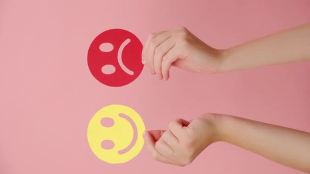 ピンクの壁に隔離された幸せで怒っている顔のペーパーを保持する女性の手の垂直ビデオ フィードバック評価 感情知能 感情コントロール メンタルヘルス評価 双極性障害の概念 — ストック動画