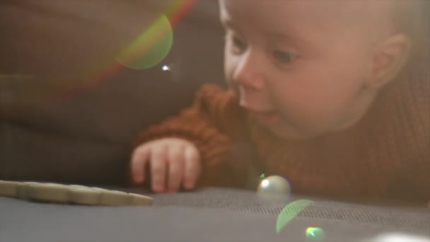 おもちゃに触れる好奇心旺盛なかわいい幼児の男の子の選択的な焦点 自宅で快適なソファに横たわり 朝のリビングルームで遊ぶ暖かい茶色のセーターでかわいい赤ちゃんの子供 育児の概念 — ストック動画
