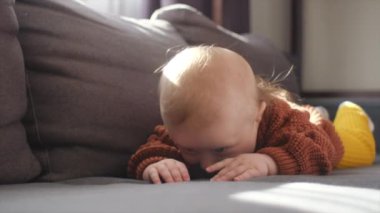 Evdeki rahat kanepede uzanmış, kahverengi örülü süveter giyen, neşeli gülümseyen kameraya doğru bakan mutlu küçük çocuğun seçici odağı. Sabah güzel bir erkek çocuk portresi.