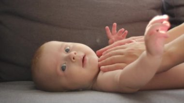 Küçük bebeğe masaj yapan anne ellerinin yakın çekimi. Bebek bakımı konsepti. Kolik önleme. Yeni doğan bebeğe masaj yapan kadın elleri. Evdeki aydınlık odada rahat bir kanepede uzanmış beyaz bir bebek.