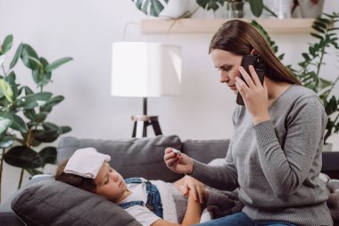 Kanepede yatan üzgün, hasta, küçük kız ateşler içinde nezle oluyor. Endişeli anne, çocuk sıcaklığını ölçtükten sonra doktor aile terapistini arıyor. Aile doktorunu arıyorum.