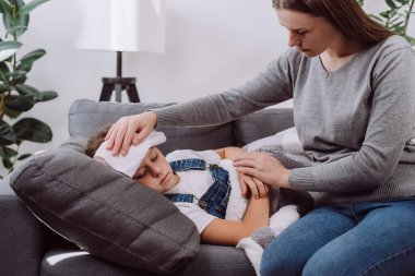 İlgili genç anne hasta küçük kızına bakıyor. Hasta çocuğun battaniyenin altında yatarken yüksek ateşi var. Bekar beyaz anne, evdeki oturma odasında hasta kıza bakıyor.