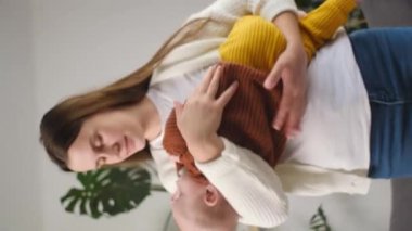 Kaygısız, gülümseyen, sevgi dolu bir annenin sevgili küçük bebeğini kucağına aldığı dikey bir video. Önemseyen mutlu anne kucağında küçük sevimli bir bebek ve komik bir çocuğu olan çocuk evde birlikte vakit geçirmenin tadını çıkarıyor. Annelik kavramı
