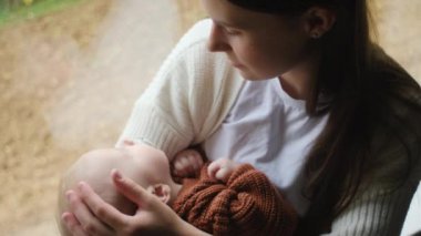 Sevgi dolu anne ve bebeğin sıcak sonbahar arka planında rahat bir pencere kenarında oturması, sıcak yanaklı tatlı bir bebekle konuşması. Şefkatli anne şımarık küçük bebek çocuğu okşuyor.