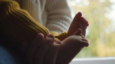 Küçük şirin bebek ayaklarını annenin ellerine bırak, küçük oğlunu kucağına al sonbahar doğası arka planında rahat pencere pervazında otur. Mutlu aile anları. Annelik ve çocukluk kavramı