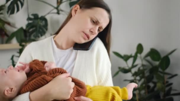Orolig Ung Mamma Hålla Nyfödda Son Händer Och Prata Smartphone — Stockvideo